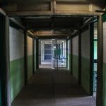 Corredor vazio de uma prisão, com portas de celas abertas e grades metálicas.
