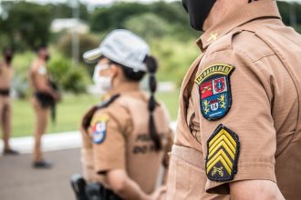 Policiais fardados permanecem em formação ao ar livre.