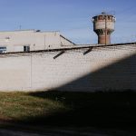Muro de presídio com arame farpado e torre de vigilância sob céu azul