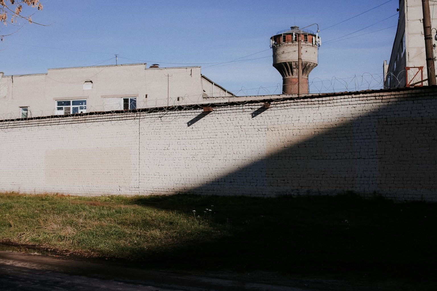Muro de presídio com arame farpado e torre de vigilância sob céu azul