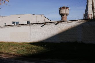 Muro de presídio com arame farpado e torre de vigilância sob céu azul