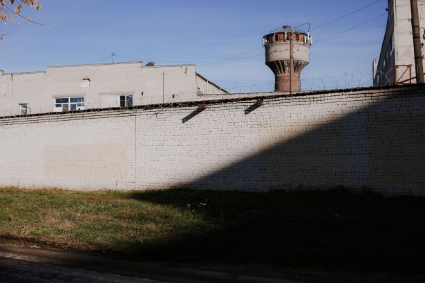 Muro de presídio com arame farpado e torre de vigilância sob céu azul